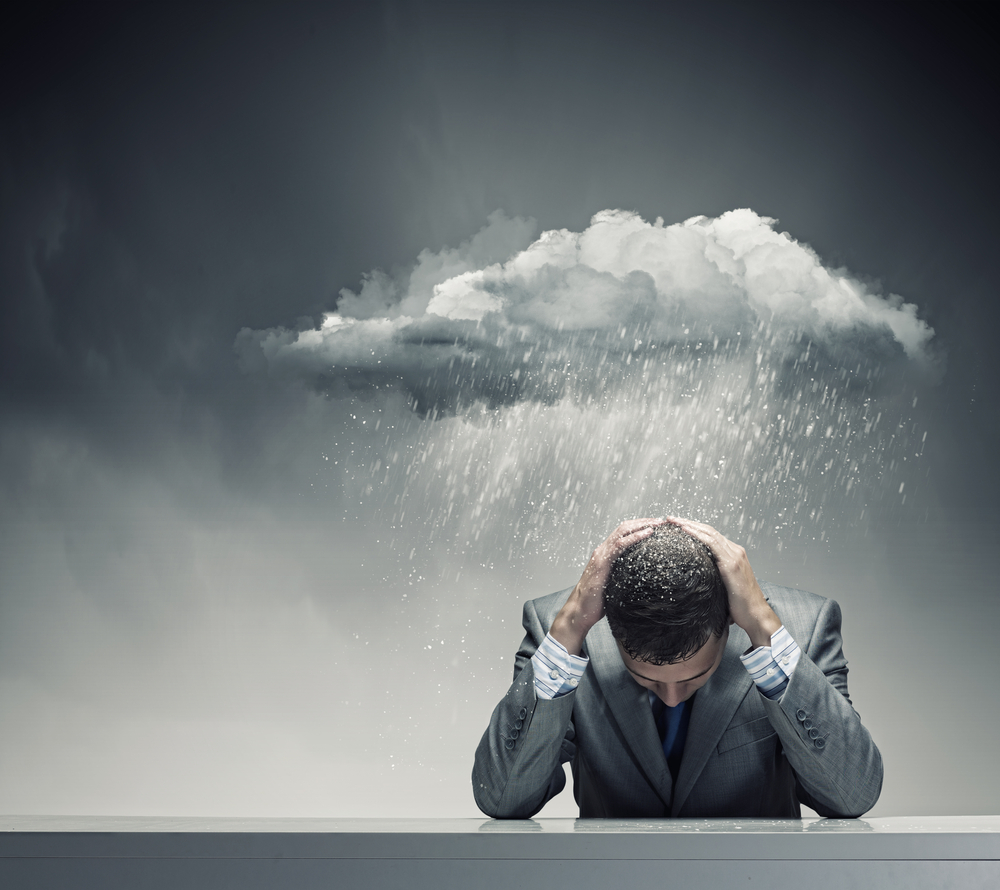 Depressed young businessman sitting wet under rain