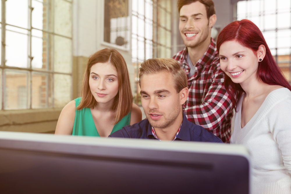 young business team watching the success of their project as they stand grouped around a large screen desktop computer