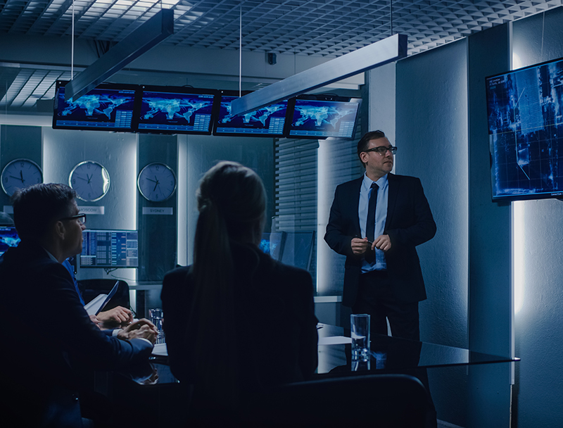 Chief of Operations Shows Surveillance Footage on Wall TV Screen to a Team