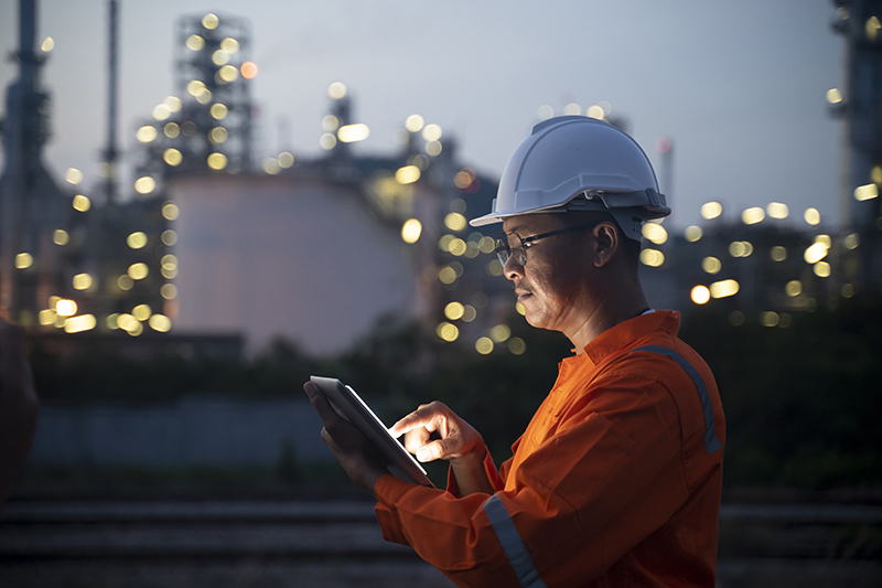 Engineer using tablet near oil refinery at night