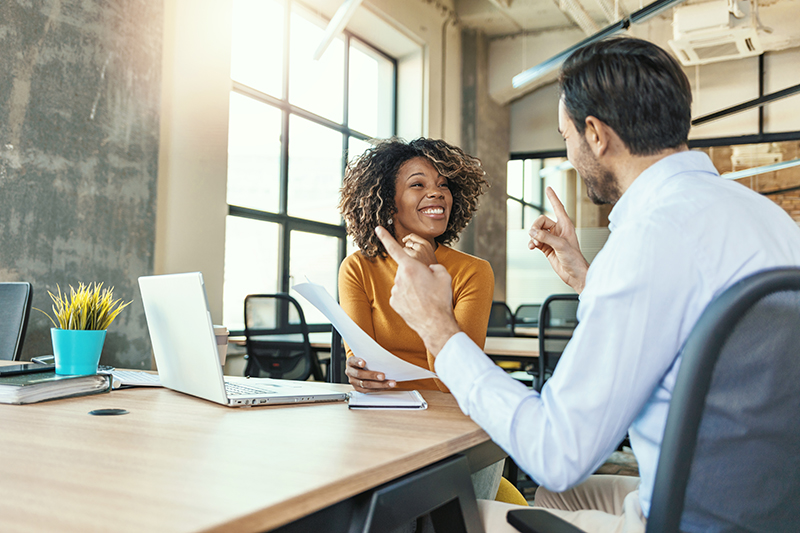 woman working with laptop with smile and discussing something with her coworker