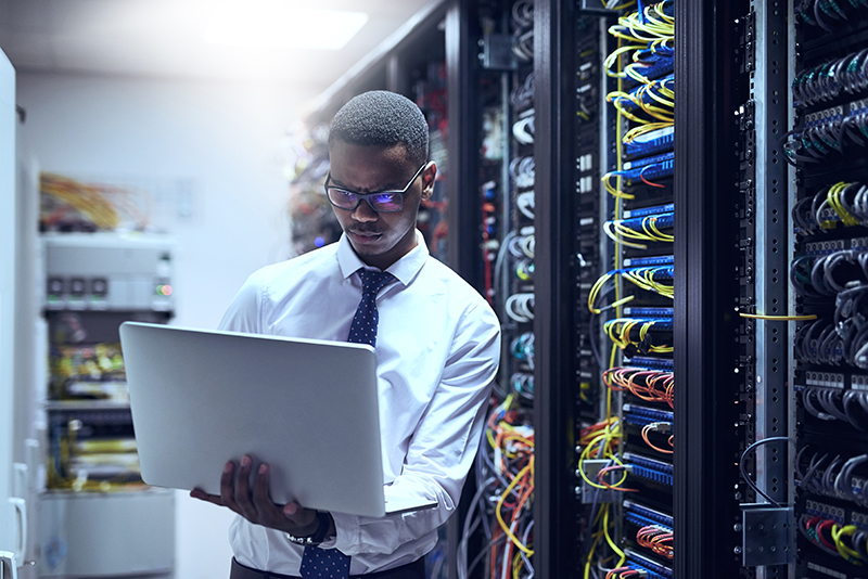 IT technician working on his laptop while standing inside of a server room