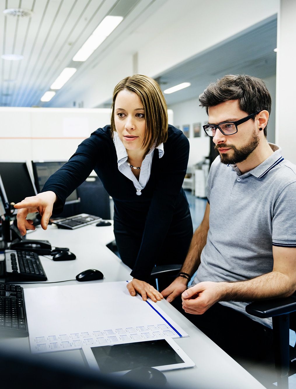 Two IT professionals in a big control room of a factory talking.