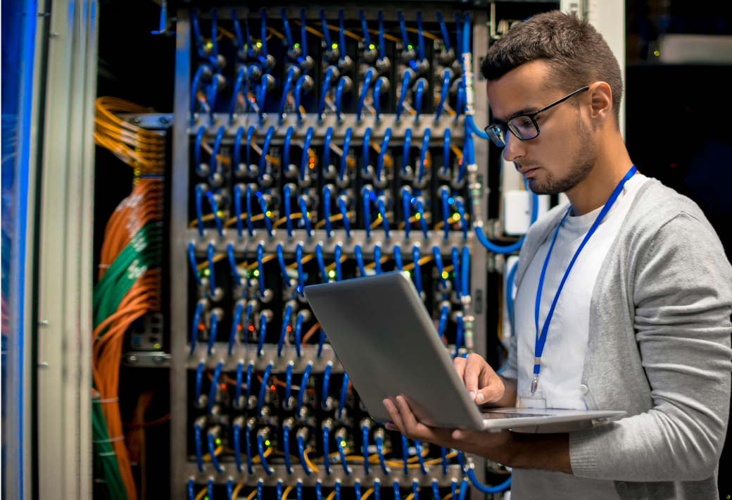 Side view portrait of young man with laptop standing by server cabinet