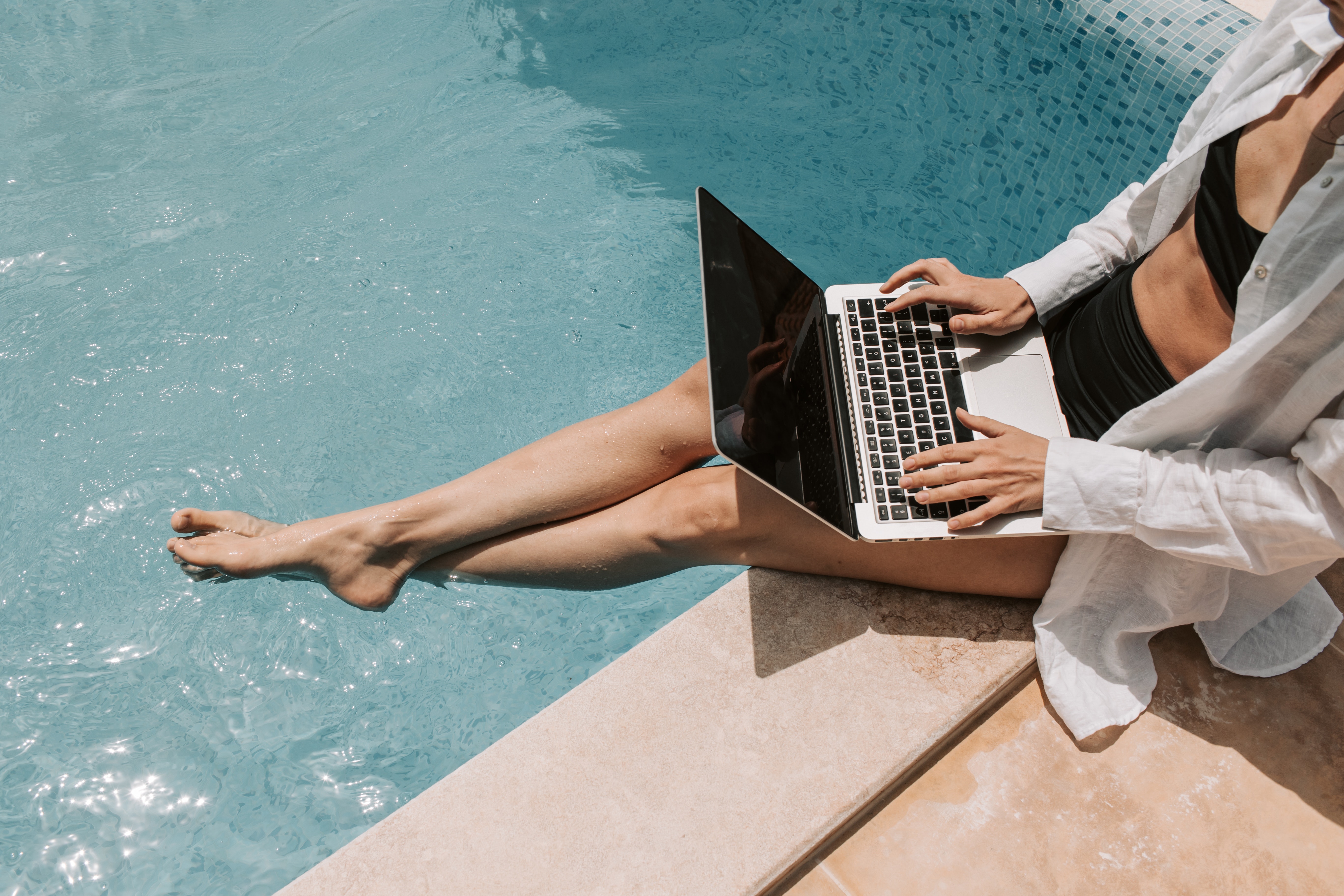 Women sitting poolside working on her laptop